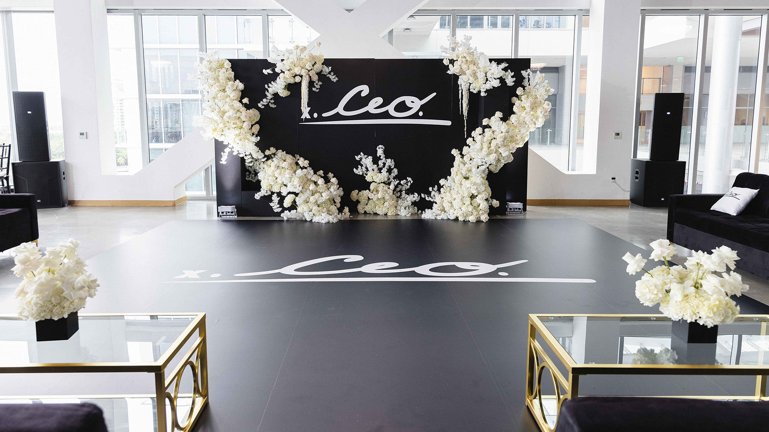 Elegant venue setup for The CEO. Ball featuring a black dance floor and floral-decorated backdrop with the CEO. Apparel logo in white.