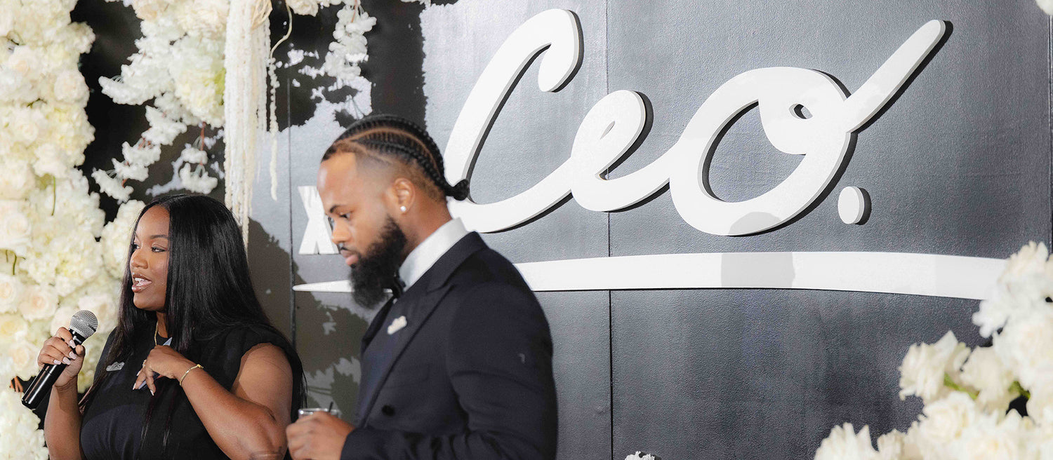 Co-founders of The CEO. Apparel speaking on stage at The CEO. Ball with a bold white logo and floral backdrop behind them.